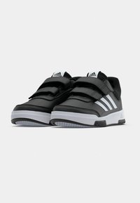 Crne Adidas tenisice s bijelim prugama i debelim bijelim potplatima, sa dva čičak traka i Adidas logom na jeziku i potplatu.