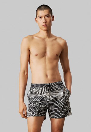 Costume da bagno a righe bianche e nere con vita regolabile, caratterizzati da linee ondulate e tasche laterali, realizzati in materiale leggero.