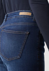 Tmavě modré denimové džíny s těsným střihem, s precizním šitím a koženou tagem na pase. Disponují klasickým pětipocket designem.