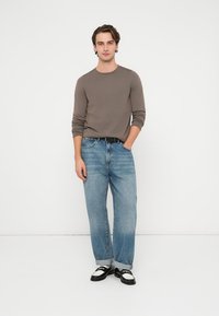 Szara koszula z długim rękawem z bawełny, zestawiona z jasnoniebieskimi, prostymi jeansami oraz czarno-białymi butami. Prosty, casualowy design z podwiniętymi mankietami.