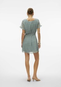 Kurzes gepunktetes Kleid aus leichtem, strukturiertem Stoff; verfügt über kurze schwingende Ärmel, eine definierte Taille und ein Rundrücken-Design.