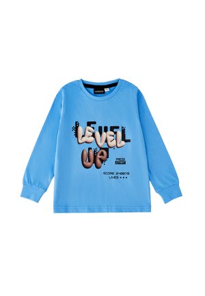 Camisa azul de manga larga con texto de temática gaming "LEVEL UP," "PRESS START," puntuación y vidas mostradas en fuente estilo píxel.