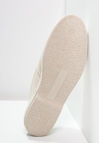 Beige instapschoen met een gestructureerde rubberen zool. De bovenkant is gemaakt van een zachte stof en heeft een subtiel patroon langs de randen. Maat 41-label zichtbaar.
