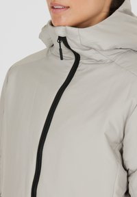 Helle graue Jacke mit hohem Kragen, Frontreißverschluss und schwarzem Reißverschluss. Glatte Textur. Verfügt über ein minimalistisches Design ohne Muster.