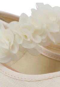 Scarpe in tessuto di colore rosa chiaro con un dettaglio floreale in tessuto bianco sporco, caratterizzate da una superficie liscia e cuciture decorative lungo i bordi.