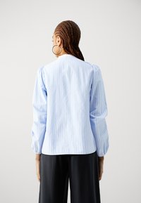 Light blue striped blouse with puffy sleeves, round neck, and smooth texture, paired with black pants. Subtle vertical pattern visible.