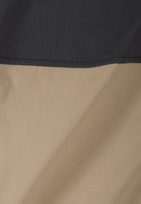 Nahaufnahme eines Stoffes, der glatte beige und schwarze Textilabschnitte mit sichtbarer diagonaler Webstruktur und einer genähten Naht zwischen den Farben zeigt.