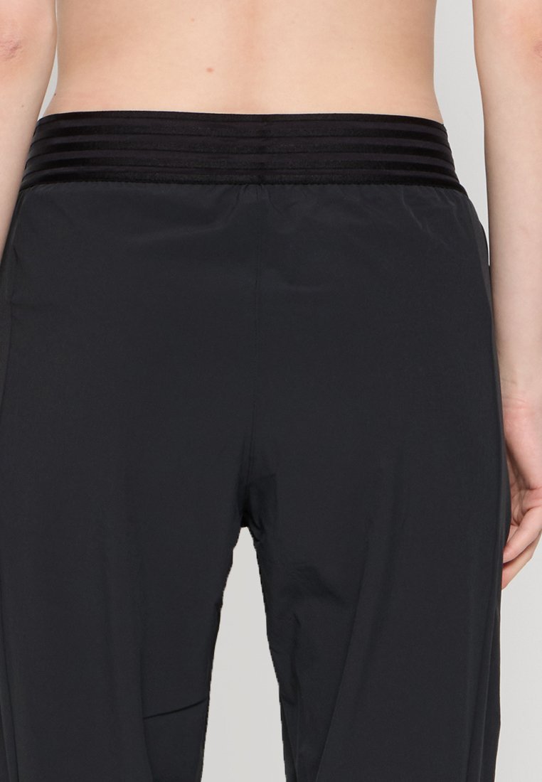 Pantalons de sport noirs avec une ceinture texturée et côtelée, dotés d'un tissu lisse et d'une coupe ample, conçus pour le confort et le mouvement.