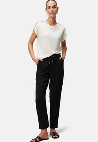 Hellgraues T-Shirt mit kurzen Ärmeln und schwarze Jogginghose mit Kordelzug. Das Outfit hat eine lockere Passform und wird mit schwarzen Slidesandalen kombiniert.