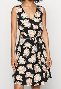 Černé květinové šaty s výstřihem do V, se broskvovými růžemi a zelenými listy. Pas je zdoben stuhou a látka má lehkou texturu.