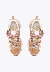 Une paire de baskets beiges et roses avec des décorations de lacets en bijoux et perles, des accents en suède beige et un bouton de marque rose sur les languettes.