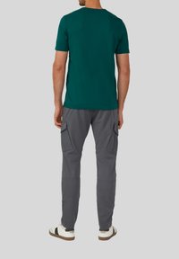 Camiseta verde de manga corta combinada con pantalones cargo grises que cuentan con bolsillos laterales y un corte ajustado. Zapatillas blancas con detalles en negro completan el look.