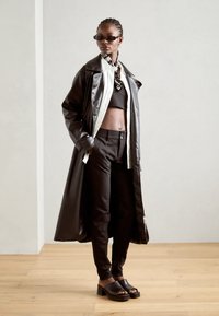 Crni kožni trench kaput preko crnog kratkog topa, krojene crne hlače i debeli crni sandali. Ima elegantne linije i minimalistički dizajn.