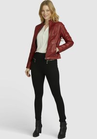 Rote Lederjacke mit tailliertem Schnitt, mit Reißverschlusstaschen und Stehkragen, kombiniert mit schwarzen Leggings und Stiefeln mit Absatz.
