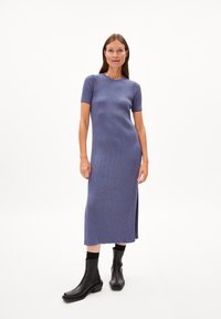 Strick-Midi-Kleid in Blau- und Lila-Streifen, kurze Ärmel, runder Ausschnitt, seitlicher Schlitz, kombiniert mit schwarzen Knöchelstiefeln. Glatte Textur.