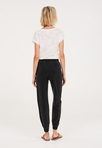 Vit, texturerad t-shirt med korta ärmar, parat med svarta, mjuka kordflöjlsbyxor med resår i benen och bakfickor.