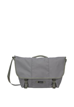 Bolsa mensajera Timbuk2 gris con cierre de solapa, correa de hombro ajustable, asa superior y dos cierres con hebilla en la parte frontal.