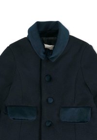 Manteau bleu marine foncé présentant une texture douce, un large col, des boutons arrondis et deux poches texturées avec une finition lisse.