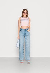 Rosa kort topp med blå logotyp, högmidjade ljusblå jeans, ljusblå handväska och blå öppna klackar. Enkel design.