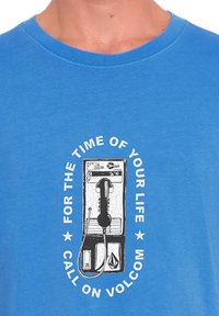 Blå bomulds T-shirt med et grafisk motiv af en vintage betalingstelefon med teksten "FOR THE TIME OF YOUR LIFE" i et sort-hvidt cirkulært design.