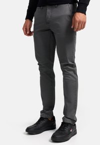 Pantalons de yoga gris en tissu tissé, dotés d'une coupe slim, d'un design à cinq poches et d'un motif texturé subtil. Baskets noires avec lacets.