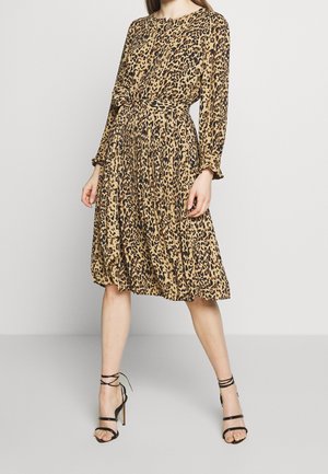 Mujer con vestido hasta la rodilla de estampado de leopardo, mangas largas y cinturón en la cintura, combinado con sandalias negras de tacón alto y tiras.