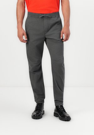 Pantalones ligeros de un gris oscuro con cintura elástica y cordón ajustable. Combinados con botas negras con cordones y suela gruesa.