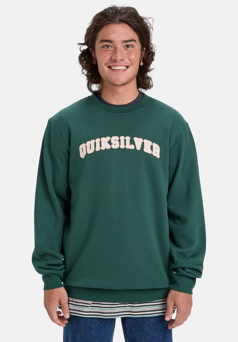 Zelený crewneck sveter s logom "QUIKSILVER" v odtieňoch krémovej, mäkká textúra, pruhované manžety a spodný lem, nosený cez pruhovanú košeľu.