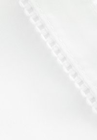 Vitt tyg med en slät textur, med en delikat spetskant på ena sidan, som har jämnt fördelade, cirkulära utskärningar.