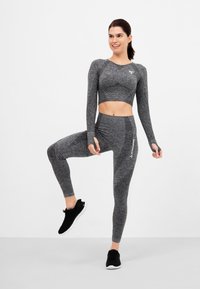 Gray athletic crop top and leggings made of textured fabric, accented with logo details. Model wears black sneakers.