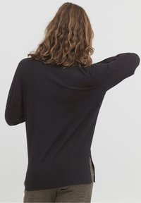 Maglione a maniche lunghe di un blu navy scuro con vestibilità rilassata, fessure laterali all'orlo e texture in maglia. La parte posteriore presenta un colletto arrotondato e spalle scese.