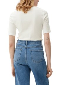 Haut blanc à manches courtes avec un col rond, associé à un jean en denim bleu clair taille haute, doté de deux poches arrières et d'une texture usée.