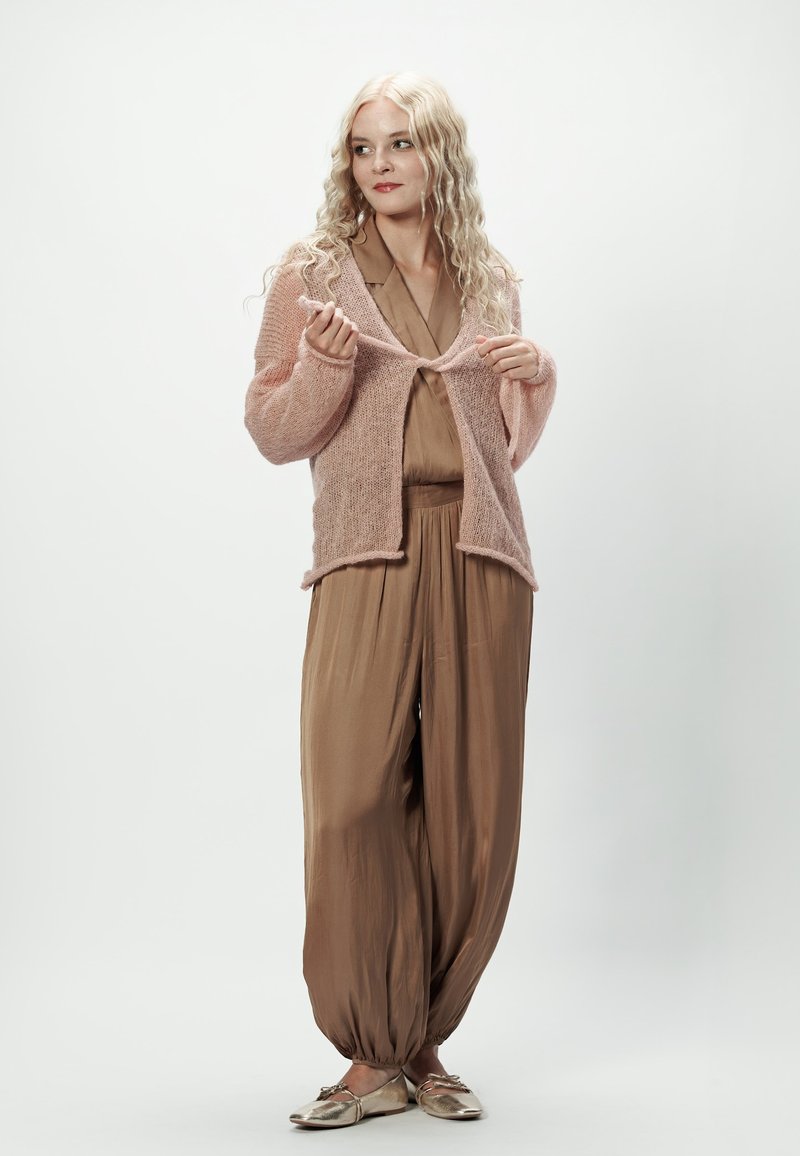 Jasnoróżowy, dziany kardigan z otwartym przodem, noszony na brązowym, jedwabnym kombinezonie. Całość dopełniają metaliczne buty.