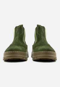 Stivaletti alla caviglia in suede verde con pannelli elastici laterali e una spessa suola in gomma beige. Presentano una punta arrotondata e dettagli di cuciture.