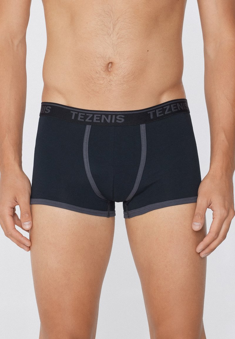 Schwarze Boxershorts aus Baumwolle mit einem grauen Gummibund, der mit dem "TEZENIS"-Logo versehen ist. Kontrastnähte entlang der Nähte.