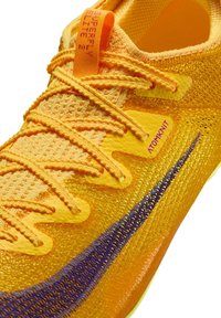 Chaussure de sport Nike avec une tige en mesh orange vif, surface texturée, bande d'accent violette et une languette de tirage jaune proéminente avec logo.