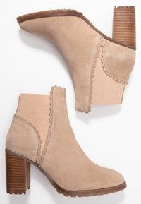 Beige mokasīni līdz potītēm no zamša ar teksturētu gumijas zoli, viļņotām malām un sablīvētu koka papēdi. Aprīkoti ar elastīgām sānu paneļiem, lai nodrošinātu piemērotību.