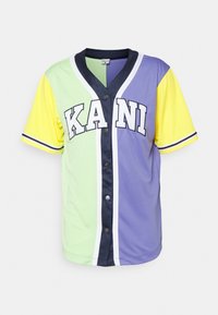 Multifarvet baseballtrøje med grønne, lavendel og gule paneler, sort knaplukning og hvide detaljer med "KANI" fremtrædende udstyret.