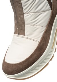 Krupni plan smeđe i kremastozimske čizme s gornjim dijelom od podstavljene tkanine, antiknim vrhom od antilopa i teksturiranim bijelim gumenim potplatom.