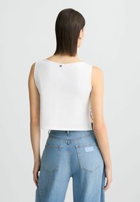 Top corto bianco con scollatura rotonda e un piccolo dettaglio con bottone sul retro, abbinato a jeans in denim azzurri a vita alta.