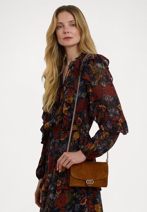Borsa a spalla in suede con una chiusura in tonalità argento, caratterizzata da un colore beige, design minimalista e tracolla a catena. Indossata su un vestito floreale con balze.