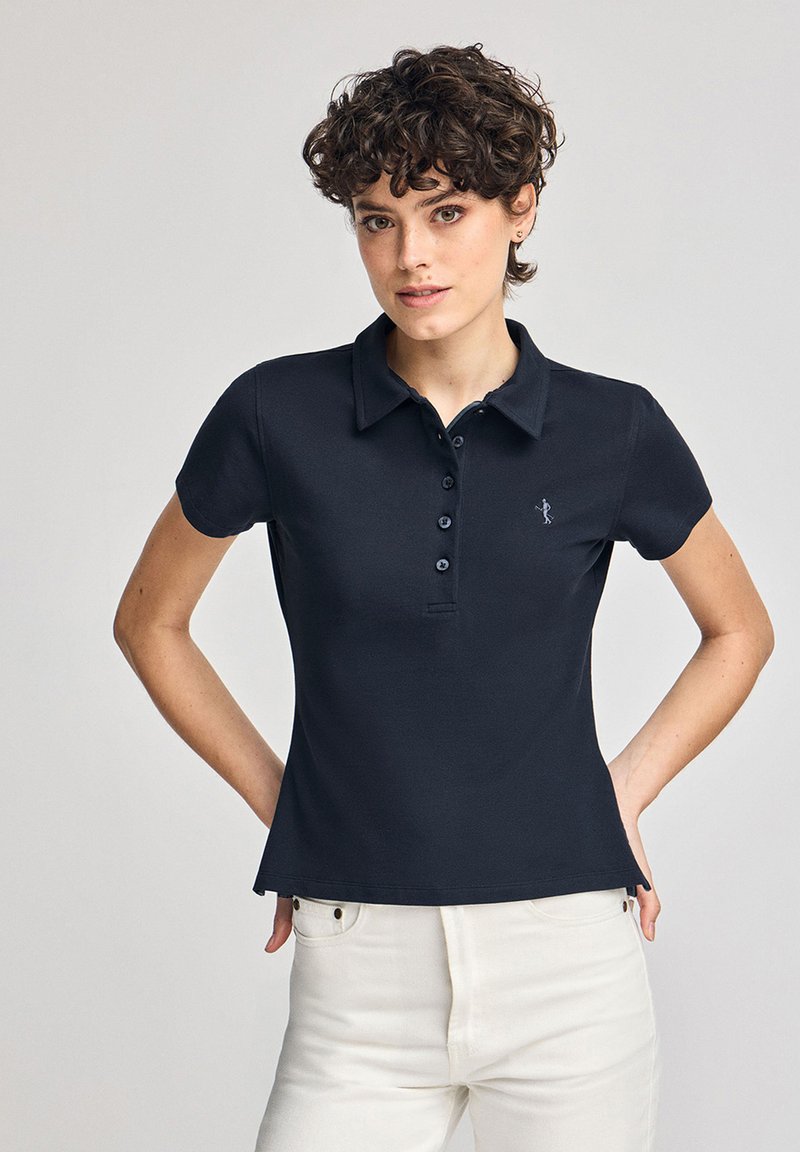 Mörkblå pikétröja i bomullstyg, med klassisk krage, fem knappar och en liten broderad logotyp på vänster bröst.