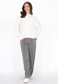 Witte, fluffy gebreide trui met een hoge hals, gecombineerd met grijze, losse broek en witte sneakers. De textuur ziet er zacht en knus uit.