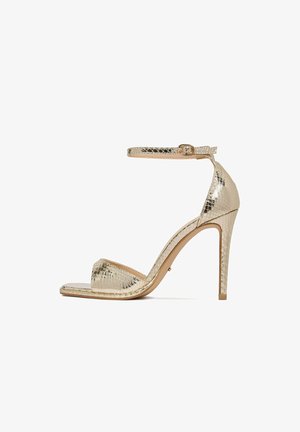 Złota sandałka na wysokim obcasie z paskiem wokół kostki i odkrytym noskiem, z fakturą przypominającą skórę węża oraz smukłym szpilkowym obcasem.