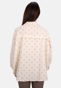 Cremfarbendes Hemd mit Blumenmuster, weicher Textur, weitem Schnitt und überschnittenen Schultern. Hellbeige Herzen gleichmäßig über den Stoff verteilt.