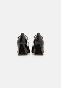 Black leather heeled shoes with a closed back and a square heel. Smooth texture with narrow ankle straps and pointed toe design.