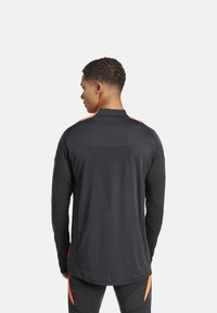 Zwart sportshirt voor mannen met lange mouwen, oranje accenten, een gestructureerd achterpatroon, hoge kraag en een aangesloten ontwerp.