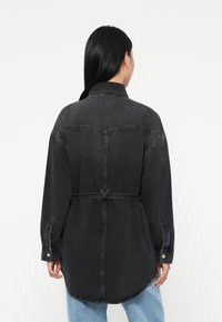 Mörkgrå denim skjortjacka med belagd midja, långa ärmar och en svängd fåll. Har en klassisk krage och diskreta sömnadsdetaljer.