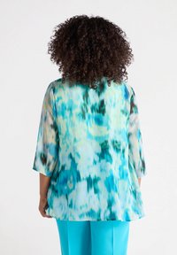 Doorzichtig blauwe top met een levendig aquarelpatroon, voorzien van driekwartmouwen en een loose fit, gecombineerd met effen turquoise broek.