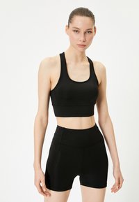 Sort atletisk crop top og høj talje shorts lavet af glat, strækbart stof. Har minimalistisk design og tætsiddende silhuet.